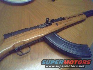 SKS rifle with banana magazine on wooden table. Supermotors.net logo