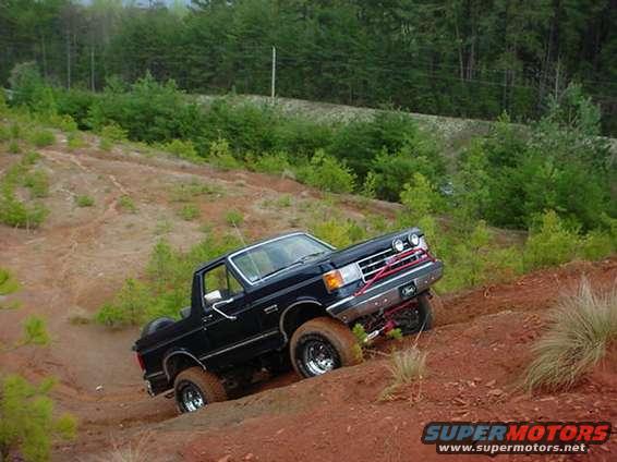 Black SUV climbing a steep dirt hill with trees in the background