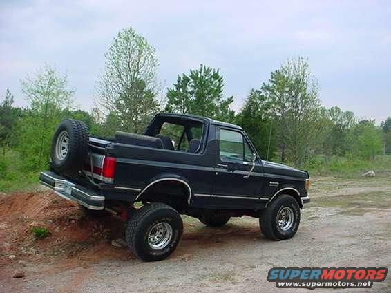 Black Ford Bronco with a spare tire mounted on the rear, angled on a dirt incline