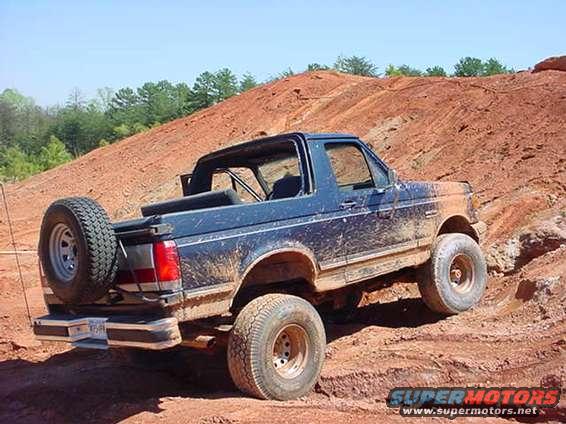1989 Ford Bronco driving on a dirt hill, covered in mud