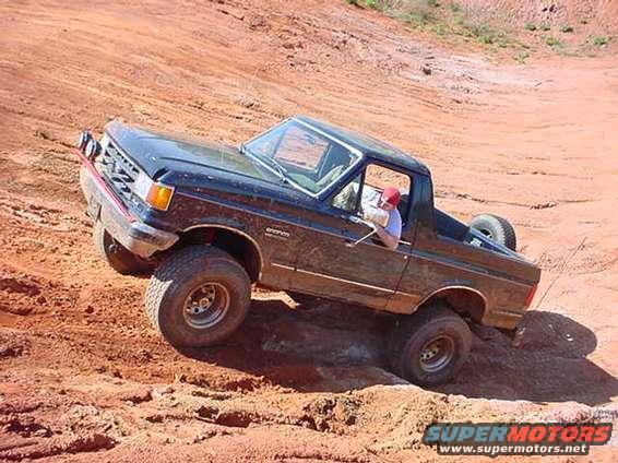 Black Ford Bronco climbing a dirt hill with one wheel off the ground