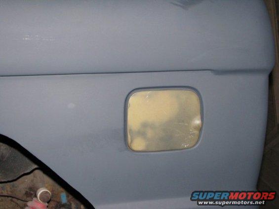 close-up of a gray vehicle body panel with a fuel door opening, showing primer underneath