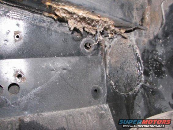 Close-up of heavily rusted and damaged vehicle frame, showing holes and corrosion