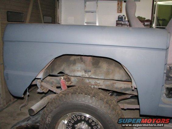 Rear fender and wheel well of a vehicle in primer, showing suspension components