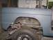 1976 Ford Bronco - The rear fender and wheel well of a vehicle, prepped for paint, reveal suspension details and a tire with a custom rim.