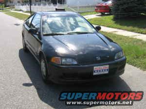 Black coupe with a dented front bumper and a cracked windshield, parked on a residential street