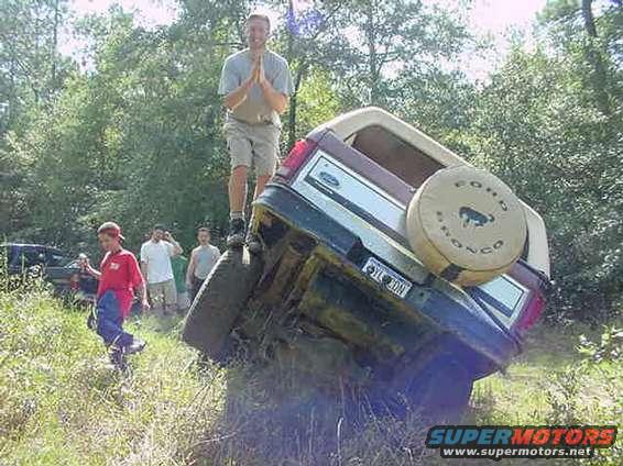 1985 Ford Bronco on its side, rear view, with a man standing on it
