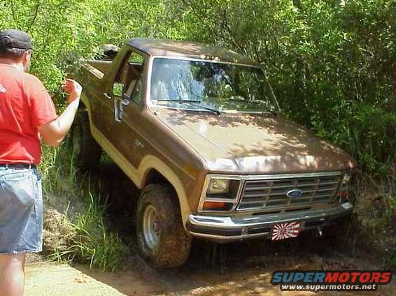 Brown 1980s Ford Bronco on a dirt trail, front 3/4 view