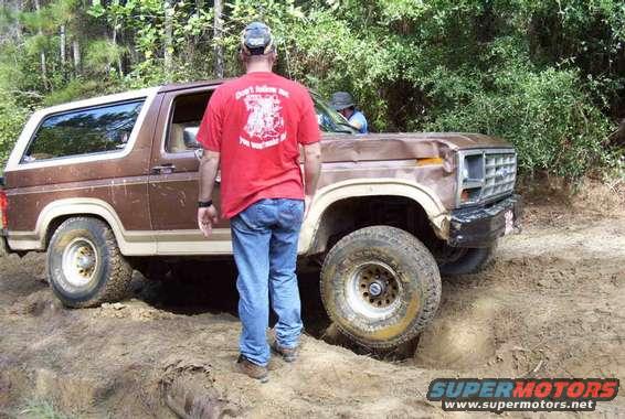 Brown Ford Bronco with a dented front fender, off-roading on a dirt trail