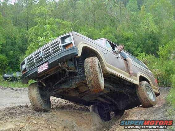 Brown Ford Bronco climbing a muddy hill, driver leaning out window