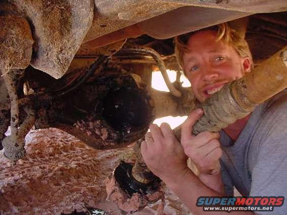 Man with driveshaft under a dirty vehicle, likely a 1980s SUV