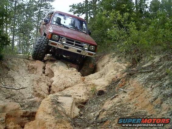 Red SUV with large tires climbing a dirt hill, front grille visible