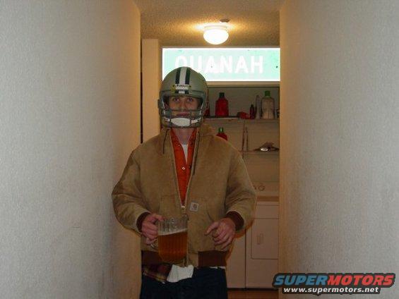 Man wearing a football helmet and a tan jacket, holding a large mug of beer