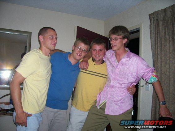 Four guys posing together indoors. One in a pink shirt has a watch