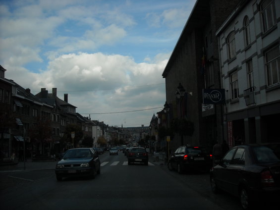 Street view in a town with buildings lining both sides and several cars driving on the road