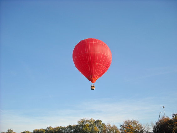 Red hot air balloon against a clear blue sky, with trees and a lamppost visible on the horizon