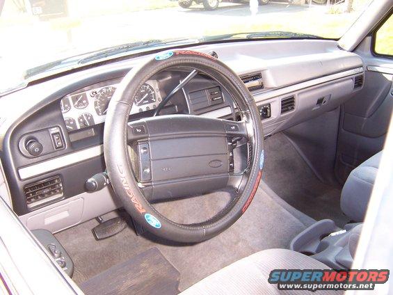 Interior shot of a truck's dashboard and steering wheel. Steering wheel has a racing-themed cover