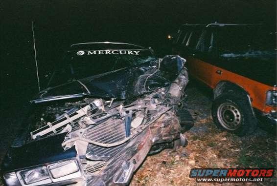 1988 Mercury Grand Marquis, heavily damaged front end, black hood with MERCURY text, parked next to an orange truck
