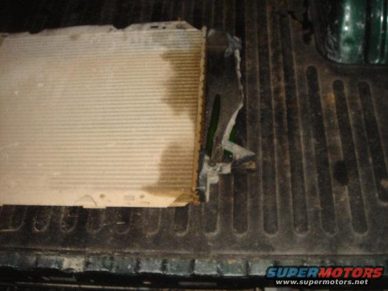 Damaged radiator with bent fins and a broken plastic side tank, resting on a ribbed surface