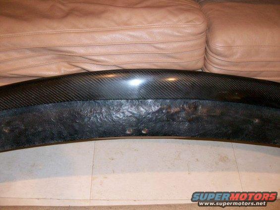 Carbon fiber car part with textured black underside, resting on a tan leather couch