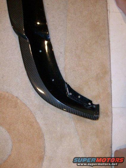 Carbon fiber car part with black glossy finish and visible weave pattern, resting on carpet