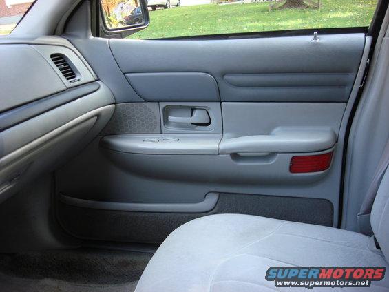 Gray interior door panel of a 2003 Ford Crown Victoria, showing the armrest, door handle, speaker grille, and window controls