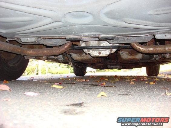 Underside of a car showing exhaust pipes, differential, and suspension components. Tires are visible on the left and right
