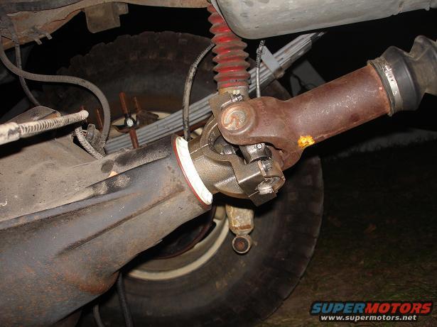 Driveshaft U-joint connected to a differential housing, with a red shock absorber and leaf springs visible