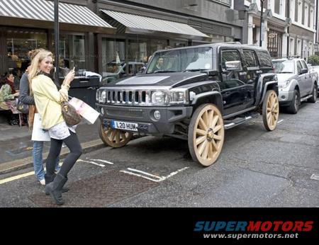 Black SUV with wooden wagon wheels parked on street, woman taking photo