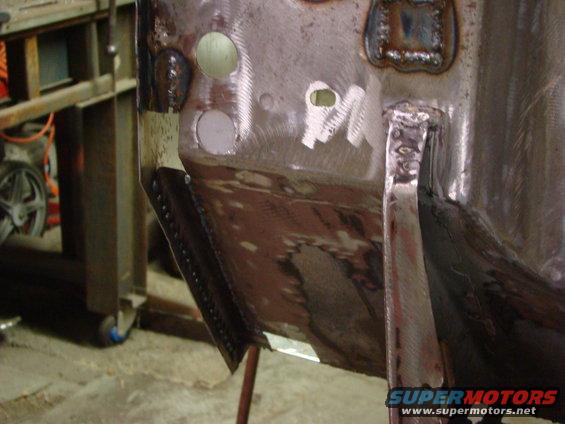 Close-up of a metal vehicle body panel undergoing repair with visible welds and grinding marks