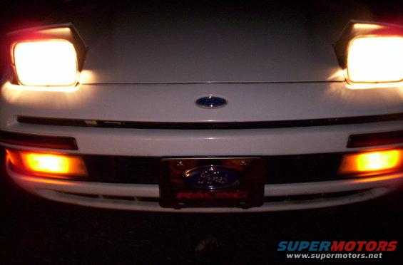 White 1991 Ford Probe front with pop-up headlights illuminated