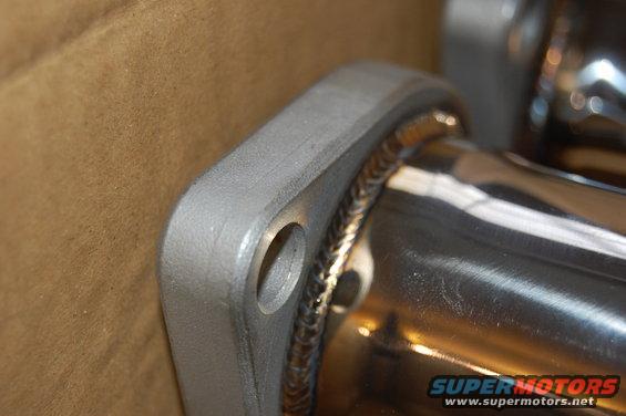 Exhaust pipe flange with two bolt holes and visible welds, against a brown background