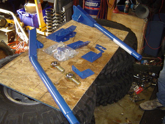 Blue suspension components and hardware laid out on a wooden surface over a large tire