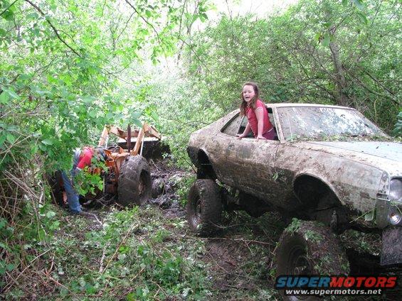 Mud-covered car with girl in window, tractor stuck in mud