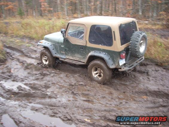 Green Jeep Wrangler with tan top stuck in deep mud, front wheel submerged