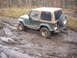 1988 Chevrolet Blazer - Jeep Wrangler navigating a muddy trail, with one wheel deep in the mire.
