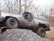 1988 Chevrolet Blazer - A driver navigates a muddy, lifted SUV over a rocky incline in a wooded area.