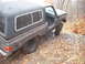 1988 Chevrolet Blazer - A dark SUV with a camper shell is tilted on a gravel path with the driver's door open.