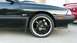 1989 Mazda MX-6 - Close-up of a black car's front fender and wheel, with another red vehicle partially visible in the background.