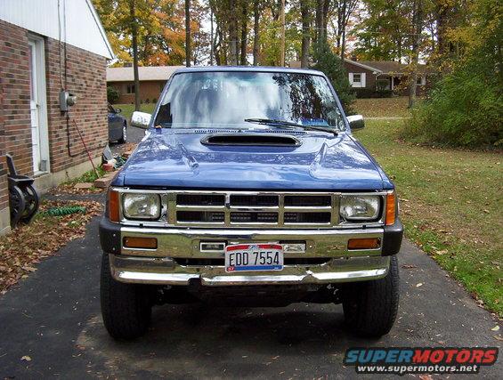 Front view of a blue pickup truck with a hood scoop and chrome bumper. License plate reads EDD 7554