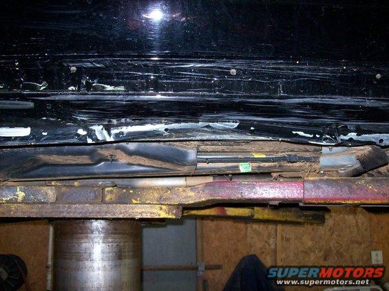 Black vehicle underbody with visible damage and rust, supported by a lift
