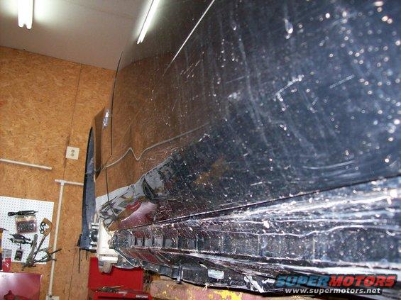 Black car side panel with significant damage and scratches, lifted on a hoist