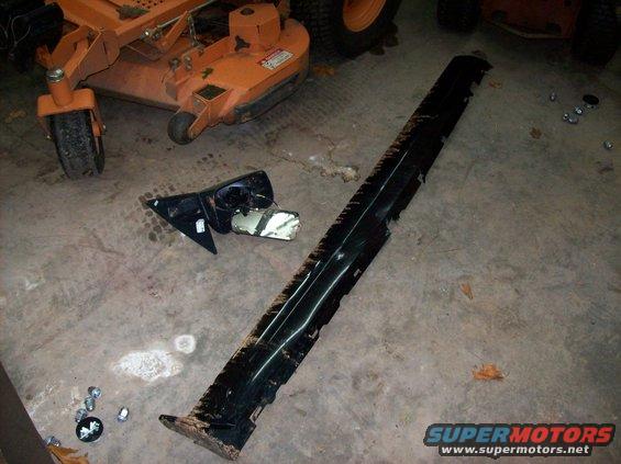 Car side skirt and side mirror on concrete floor next to lawn mower