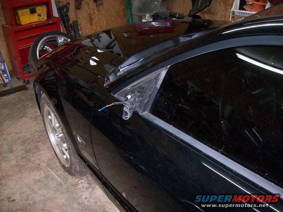 Black car with detached side mirror, showing wiring, in a garage