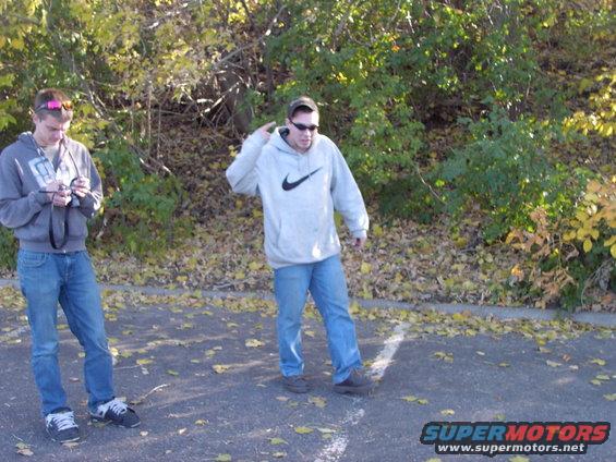 Two guys stand around outside, one on his phone, the other talking on his phone
