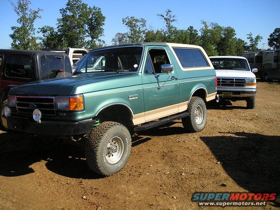 Green 1989 Ford Bronco with tan side trim and off-road tires, parked on dirt lot