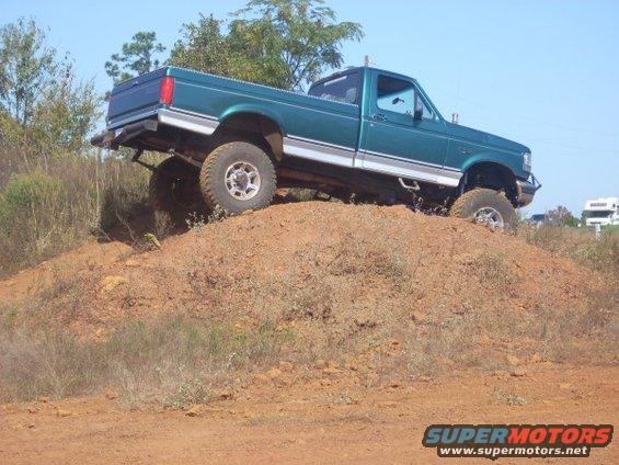 Green pickup truck climbing a dirt hill. It has large tires and a lifted suspension
