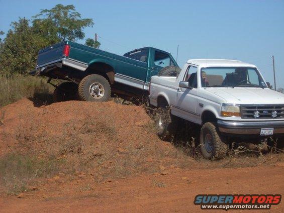 White 1992 Ford Bronco and green Ford F-150 off-roading on a dirt hill