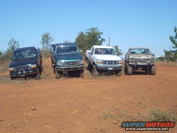 Four pickup trucks parked on a dirt hill. The trucks appear to be Ford Broncos from the early 1990s