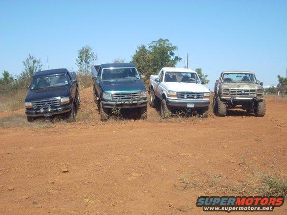 Four pickup trucks parked on a dirt hill. The trucks appear to be from the 1990s